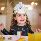 Child wearing a colorful princess crown with a blurred indoor background