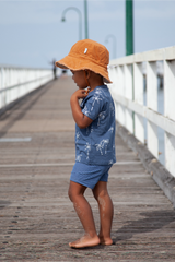 Child wearing a blue outfit with white patterns and an orange hat on a wooden pier.