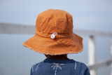 Back view of a child wearing an orange bucket hat with a blurred background