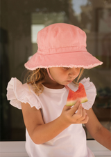 Young girl wearing a pink sun hat and white dress, eating watermelon.