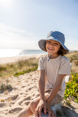 Child sitting on a sandy beach wearing a sun hat and smiling.