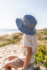 Child sitting on a sandy beach wearing a blue bucket hat.