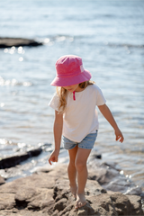 Child wearing a pink hat and white shirt standing on rocks by the water
