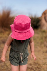 Child wearing a pink bucket hat and green outfit in a natural setting
