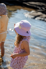 Child wearing a lavender sun hat by a body of water