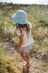 Back view of child wearing a light blue bucket hat walking in a field