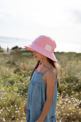 Girl wearing a pink bucket hat and blue dress standing in a field.