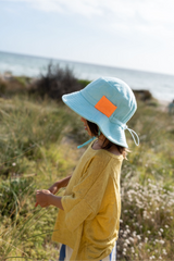 Child wearing a light blue sun hat with an orange patch in a natural setting