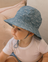 Child wearing a blue patterned sun hat sitting on a pink cushion.