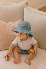 Child wearing a blue sun hat playing with wooden toys on a couch.