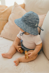 Baby sitting on a couch wearing a blue hat and playing with wooden toys.