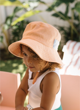 Child wearing a peach bucket hat with a plant in the background