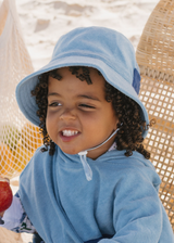 Child wearing a blue sun hat and towel, sitting outdoors.