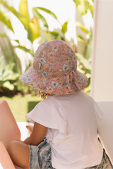 Back view of Child wearing a floral bucket hat sitting outdoors with greenery in the background