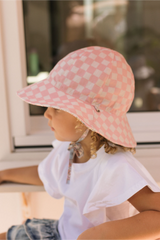 Side view of Child wearing a pink checkered sun hat sitting by a window.