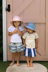 Two children wearing hats standing in front of a wooden door.