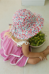 Top view of child wearing a floral hat and pink dress sitting on the floor with a bowl of grapes.