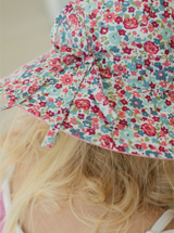 Detail view of tie on a floral sun hat worn by a child with blonde hair