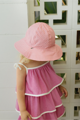Child wearing a pink dress and sun hat against a white lattice background