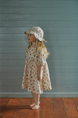 Young girl wearing a strawberry dress and hat against a teal wall.