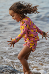 Child in a pink and yellow swimsuit playing on a beach