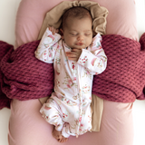 Newborn baby in a floral outfit lying on pink pillows with a purple blanket
