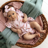 Baby in a floral outfit lying in a wicker basket with pink and green blankets.