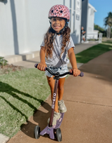 Child riding a scooter on a sidewalk with a helmet on