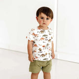 Child wearing a dinosaur-patterned shirt and green shorts on a white background
