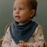 Child wearing a blue bib with a floral-patterned outfit against a green background
