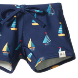 Detail view of navy blue swim shorts with sailboat pattern on a white background