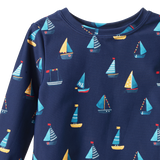 Detail view of navy blue long-sleeve swim top with colourful sailboat pattern on a white background