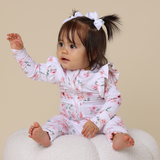 Baby in a floral outfit sitting on a white surface with a beige background