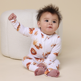 Baby wearing a white onesie with lion prints sitting on a beige surface.
