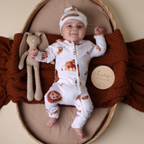 Baby in a lion-themed outfit lying on a brown blanket with a stuffed toy