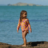Child in a colourful swimsuit standing on a rocky beach with ocean and island in the background