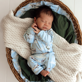 Baby lying on a cream blanket wearing a blue onesie with aircraft print