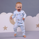 Child wearing a light blue onesie with airplane pattern against a grey wall background