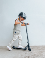 Child riding a scooter with a helmet on a plain background