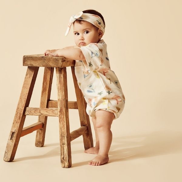 Baby standing by stool wearing WILSON & FRENCHY Cookie Cut Organic Growsuit
