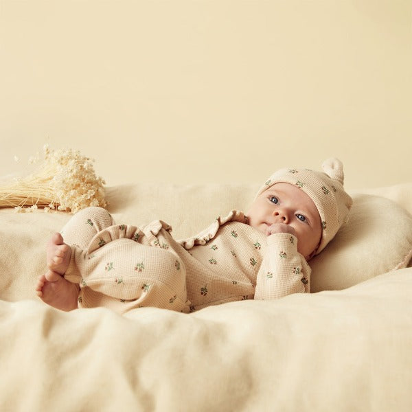Baby lying down wearing WILSON + FRENCHY Emily Floral Organic Waffle Ruffle Zipsuit