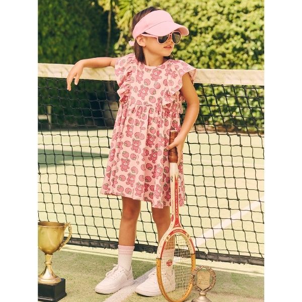 Girl holding tennis raquet by tennis net wearing the HUXBABY Berry Bear Frill Dress with Pink cap and sunglasses