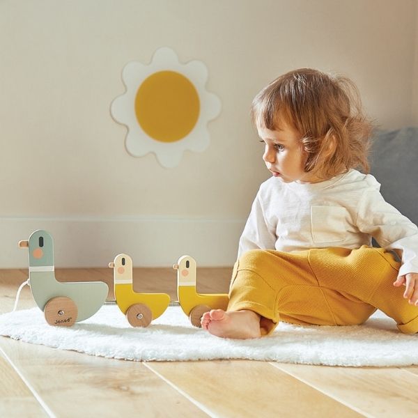 Child sitting on floor playing with the JANOD COCOON Pull Along Ducks