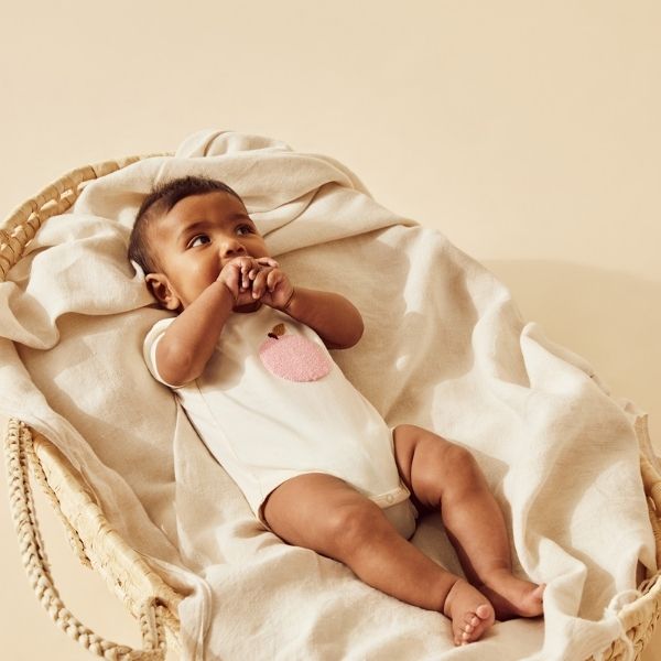 Baby lying in moses basket wearing WILSON & FRENCHY Peachy Organic Bodysuit