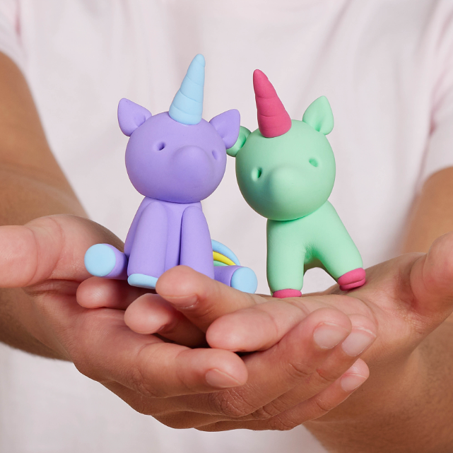Two colorful unicorn toys held in hands against a plain background