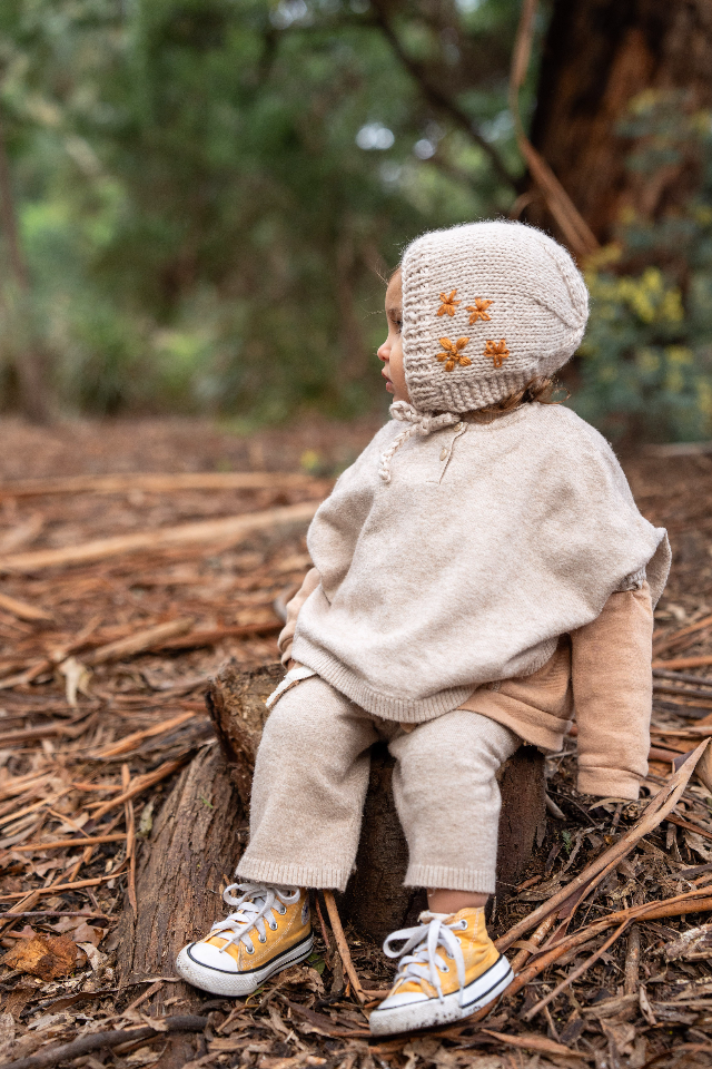 Side view of Toddler sitting on log wearing ACORN Flowers Bonnet Oatmeal 