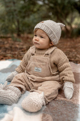 Baby sitting on rug wearing ACORN Cottontail Beanie Oatmeal and booties