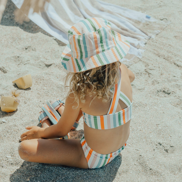 Child sitting at beach wearing CRYWOLF Bikini - Summer Stripe and matching reversible bucket hat - back view