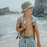 Boy at beach wearing block green side of CRYWOLF Reversible Bucket Hat - Coastal Stripe and boardies