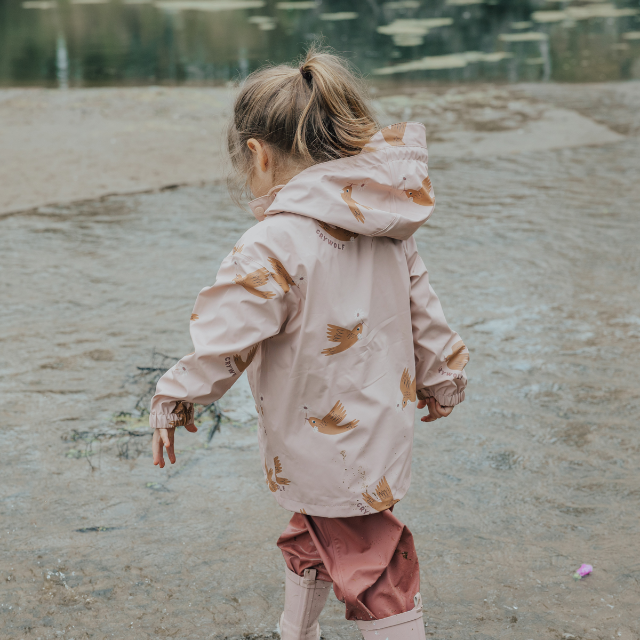 Side view of child wearing CRYWOLF Play Jacket Tui, Rosewood Rain Overalls and Dusty Pink Rain Boots